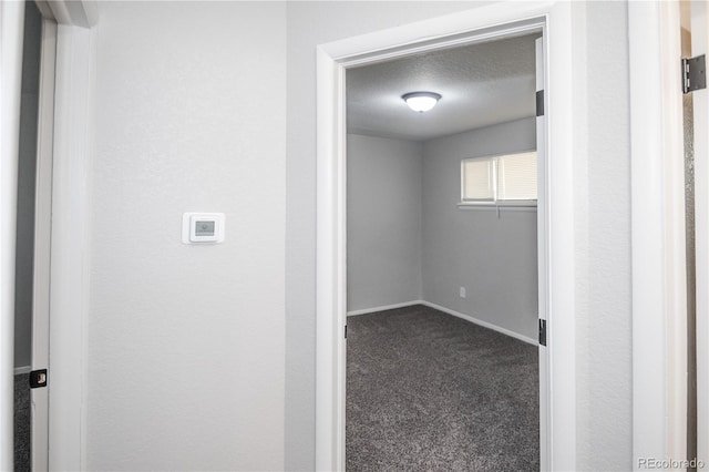 corridor with a textured ceiling and dark carpet