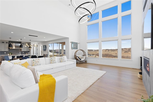 living area featuring recessed lighting, a warm lit fireplace, a high ceiling, light wood-style floors, and a notable chandelier