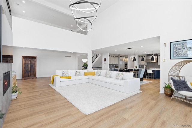 living room with light wood finished floors, visible vents, stairway, a notable chandelier, and a glass covered fireplace