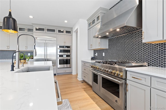 kitchen featuring a sink, decorative light fixtures, wall chimney range hood, high quality appliances, and light wood-type flooring