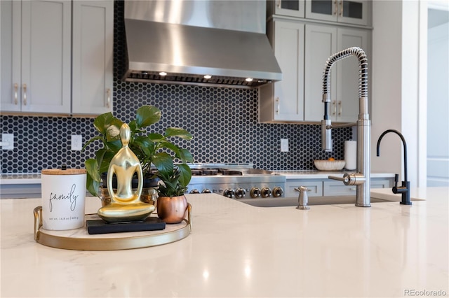 interior details with light countertops, wall chimney exhaust hood, backsplash, and gray cabinetry