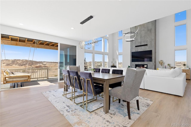 dining space featuring a tiled fireplace, wood finished floors, a towering ceiling, and a chandelier