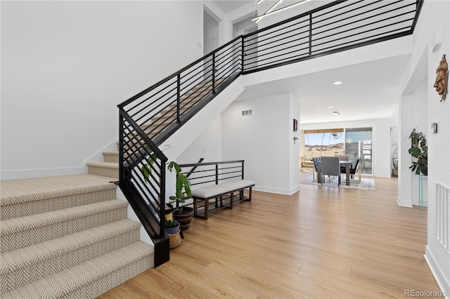 stairway featuring wood finished floors, visible vents, a towering ceiling, and baseboards