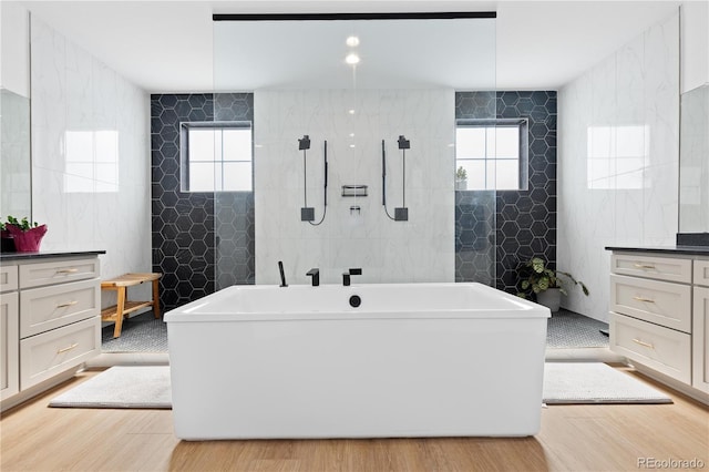 full bathroom featuring a wealth of natural light, tile walls, and wood finished floors