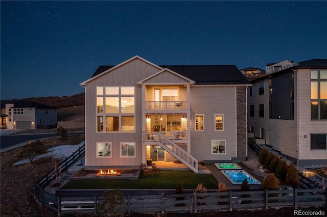 back of house at twilight featuring a balcony, stairway, an outdoor fire pit, a fenced front yard, and board and batten siding