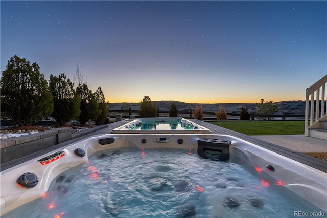 pool at dusk featuring a yard and a hot tub