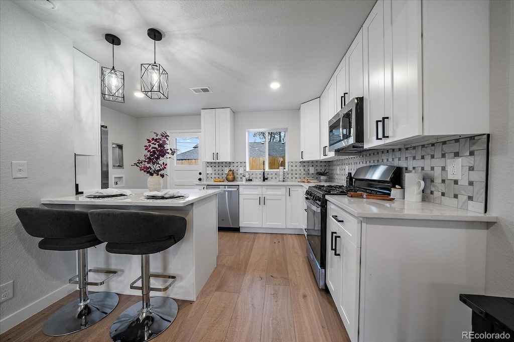 kitchen featuring pendant lighting, appliances with stainless steel finishes, white cabinetry, a kitchen breakfast bar, and kitchen peninsula