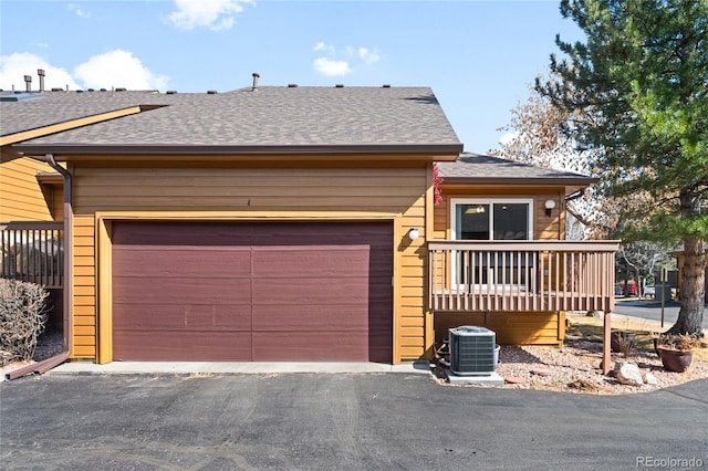 view of front of house with aphalt driveway, an attached garage, central AC, and a shingled roof