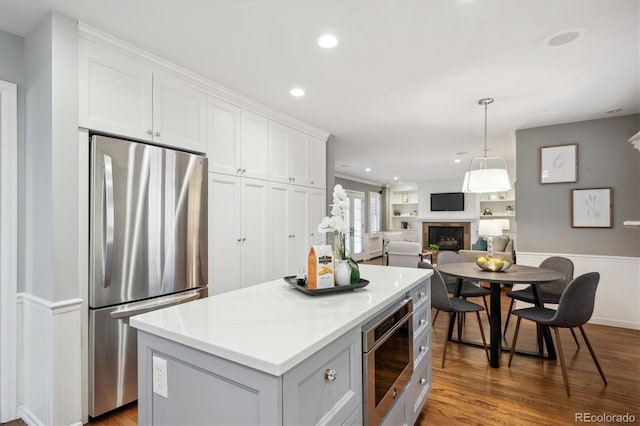 kitchen with a fireplace, appliances with stainless steel finishes, white cabinets, a kitchen island, and wood finished floors