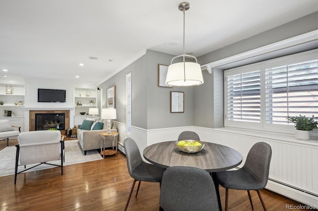 dining room with a baseboard radiator, built in features, wood finished floors, and a tile fireplace