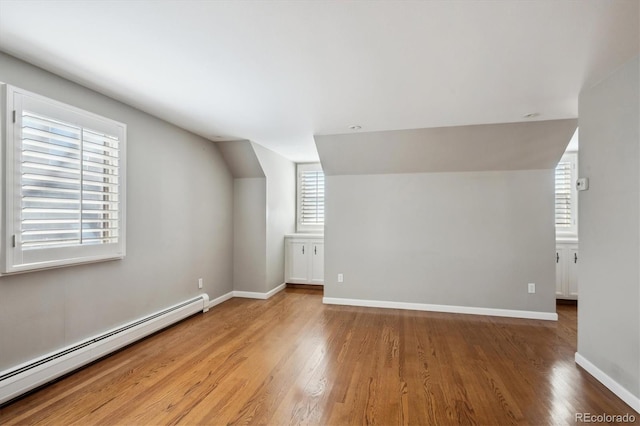 bonus room featuring a baseboard heating unit, vaulted ceiling, baseboards, and wood finished floors