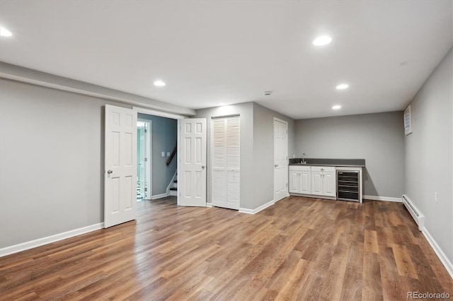 finished below grade area featuring indoor wet bar, a baseboard heating unit, wood finished floors, beverage cooler, and baseboards