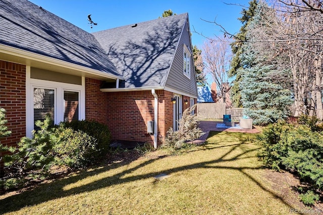 view of home's exterior featuring brick siding, roof with shingles, a lawn, a patio area, and fence