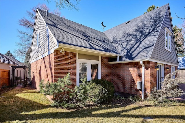 view of home's exterior featuring a yard, brick siding, a shingled roof, and fence