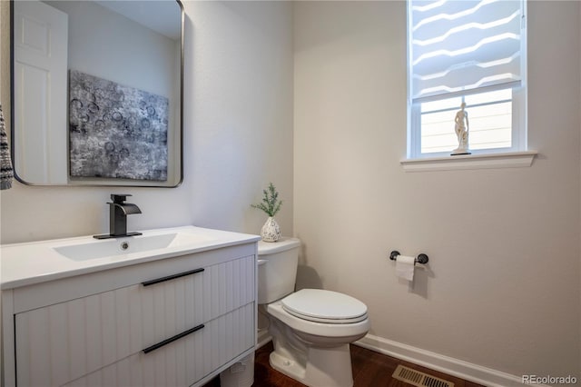 half bath featuring toilet, baseboards, visible vents, vanity, and wood finished floors