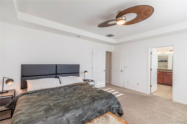 bedroom with a tray ceiling, light colored carpet, baseboards, and visible vents