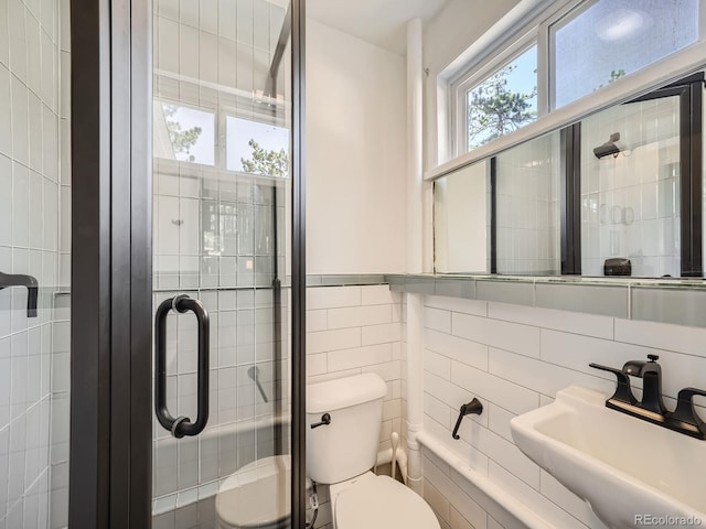 bathroom featuring sink, toilet, tile walls, and a shower with shower door