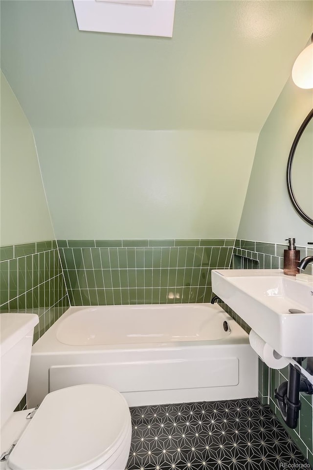 bathroom featuring toilet, tile patterned flooring, a bathtub, vaulted ceiling, and tile walls