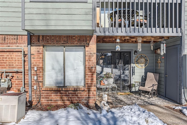 snow covered property entrance featuring cooling unit and a balcony