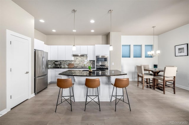 1928 W 67th Pl, Denver, CO 80221 - kitchen featuring appliances with stainless steel finishes, a breakfast bar area, a center island, decorative backsplash, and white cabinetry