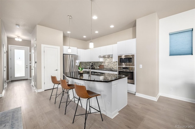 1928 W 67th Pl, Denver, CO 80221 - kitchen featuring stainless steel appliances, a sink, under cabinet range hood, dark countertops, and a kitchen bar