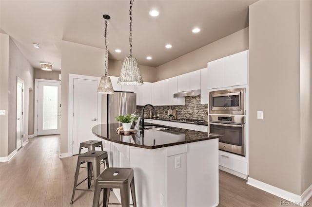 1928 W 67th Pl, Denver, CO 80221 - kitchen featuring appliances with stainless steel finishes, a breakfast bar area, tasteful backsplash, white cabinetry, and light wood-style floors