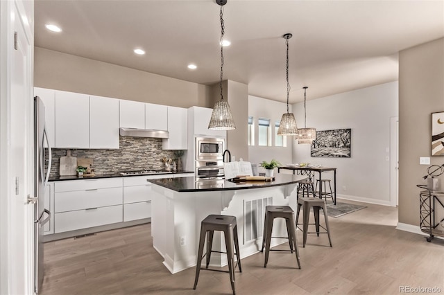 1928 W 67th Pl, Denver, CO 80221 - kitchen with a breakfast bar area, backsplash, appliances with stainless steel finishes, a kitchen island with sink, and dark countertops