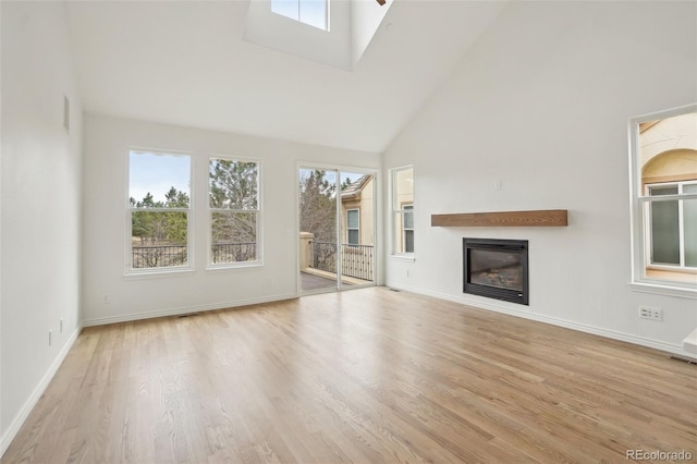 unfurnished living room featuring high vaulted ceiling, wood finished floors, a glass covered fireplace, and baseboards