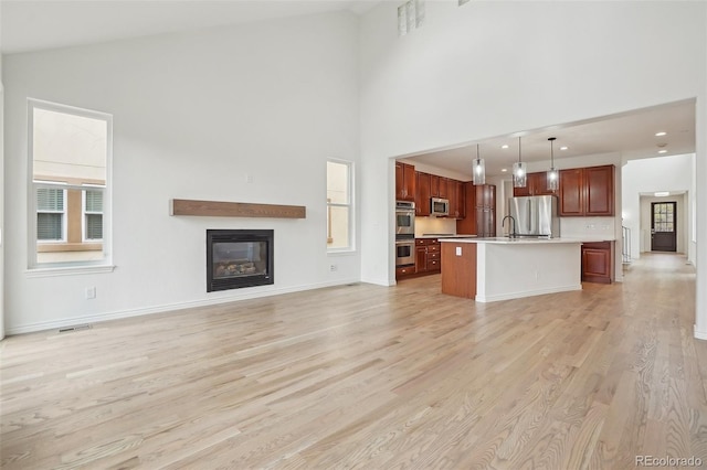 unfurnished living room with high vaulted ceiling, light wood-style flooring, a sink, baseboards, and a glass covered fireplace