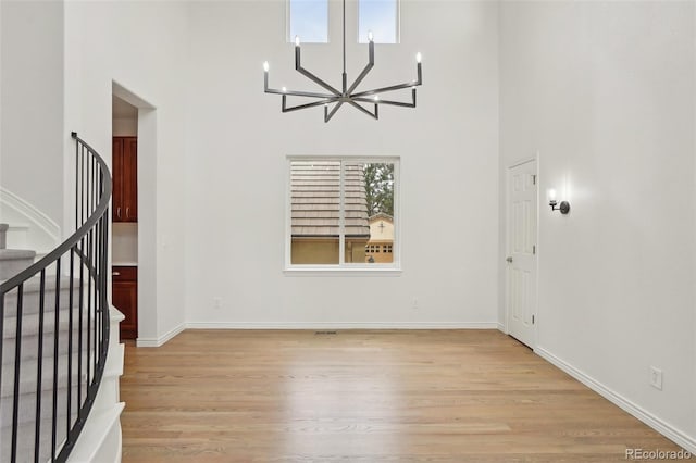 entryway featuring a high ceiling, stairway, light wood-type flooring, and an inviting chandelier