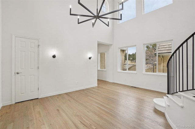 unfurnished living room featuring a notable chandelier, a high ceiling, wood finished floors, baseboards, and stairway