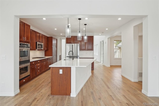 kitchen featuring pendant lighting, light countertops, backsplash, appliances with stainless steel finishes, and light wood-style floors