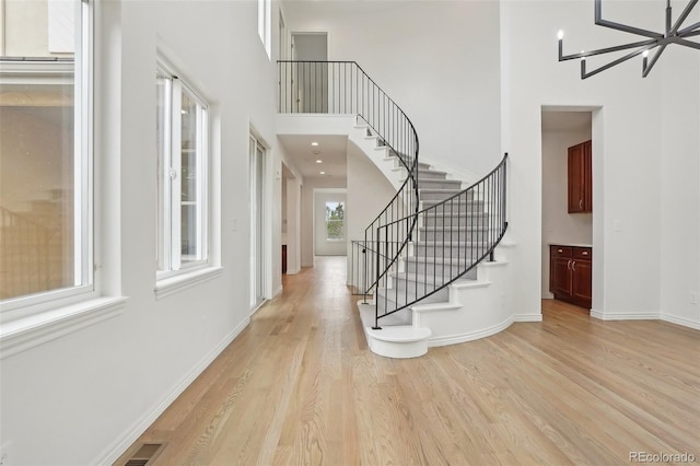 entrance foyer featuring a towering ceiling, visible vents, stairs, baseboards, and light wood finished floors