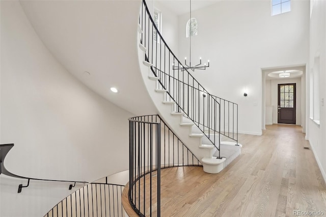 stairway featuring a high ceiling, baseboards, a chandelier, and wood finished floors