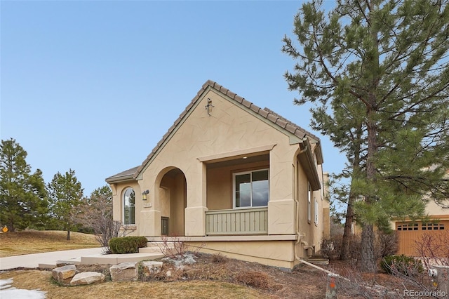 view of front facade featuring covered porch, a tile roof, and stucco siding