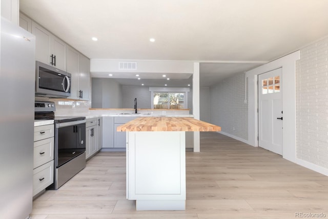 kitchen with sink, wooden counters, appliances with stainless steel finishes, backsplash, and a center island