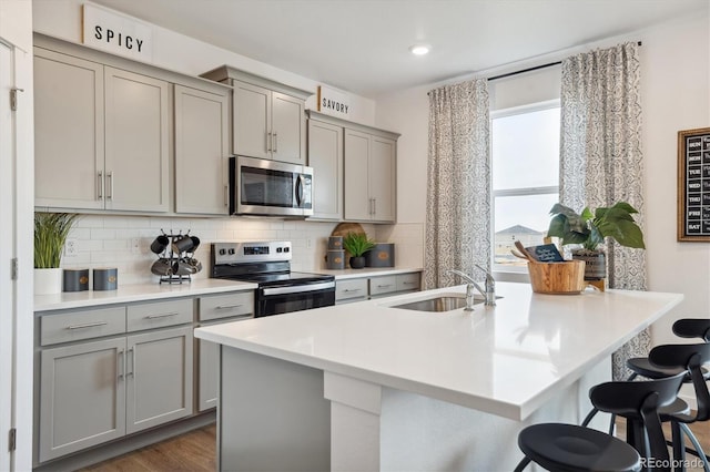 kitchen with sink, an island with sink, gray cabinetry, a breakfast bar area, and stainless steel appliances