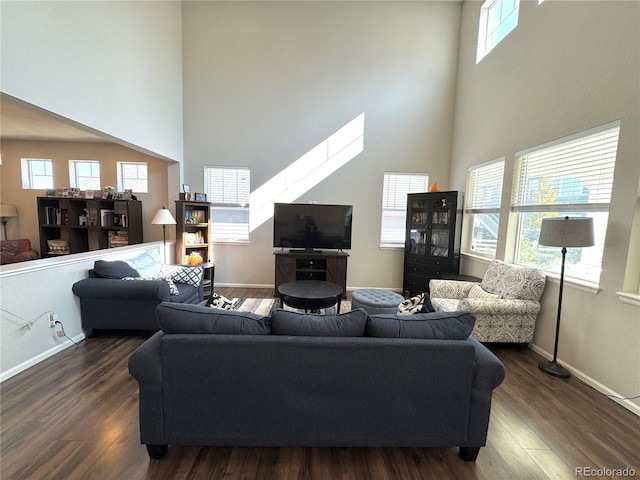 living room featuring a towering ceiling, dark wood-type flooring, and a healthy amount of sunlight