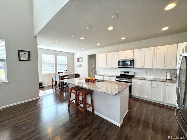 kitchen featuring dark hardwood / wood-style floors, sink, an island with sink, white cabinetry, and stainless steel appliances