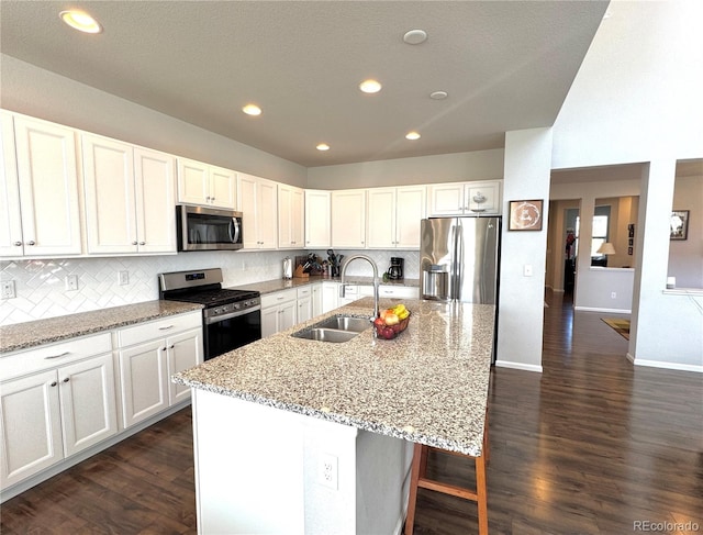 kitchen featuring dark wood-type flooring, light stone counters, stainless steel appliances, a center island with sink, and sink