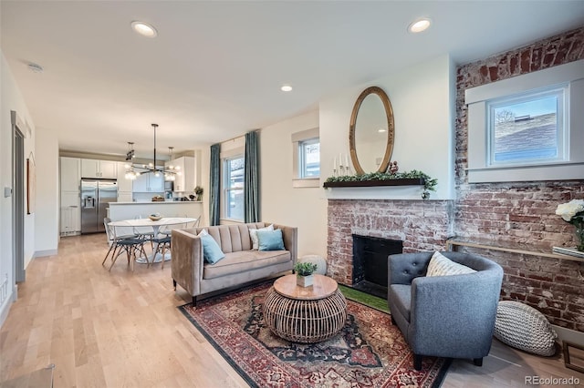 living room featuring recessed lighting, an inviting chandelier, a brick fireplace, and light wood-style floors