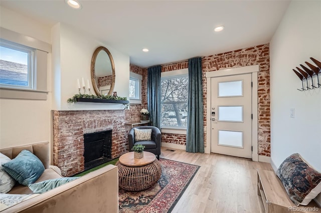 interior space with a brick fireplace, plenty of natural light, wood finished floors, and brick wall