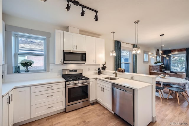 kitchen with a sink, light wood-type flooring, appliances with stainless steel finishes, and a peninsula