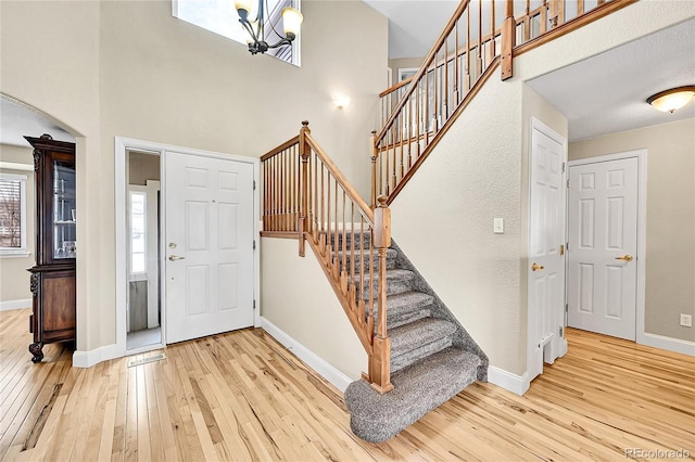 foyer entrance featuring wood-type flooring, a high ceiling, baseboards, and an inviting chandelier