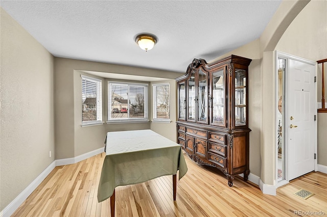 interior space with light wood-type flooring, baseboards, arched walkways, and a textured ceiling