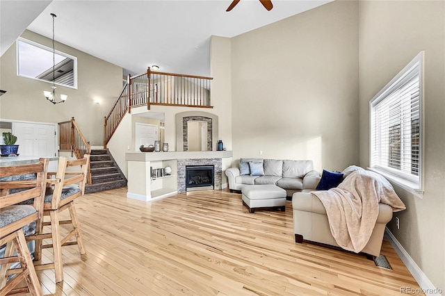 living area with baseboards, a towering ceiling, stairway, a stone fireplace, and light wood-style floors