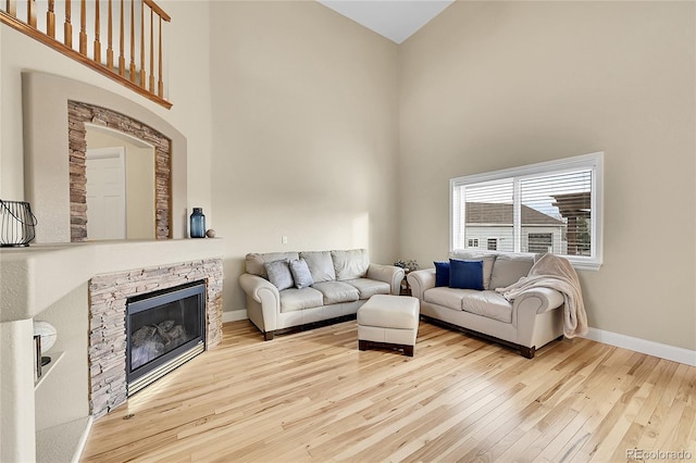 living room with wood-type flooring, baseboards, a fireplace, and a high ceiling