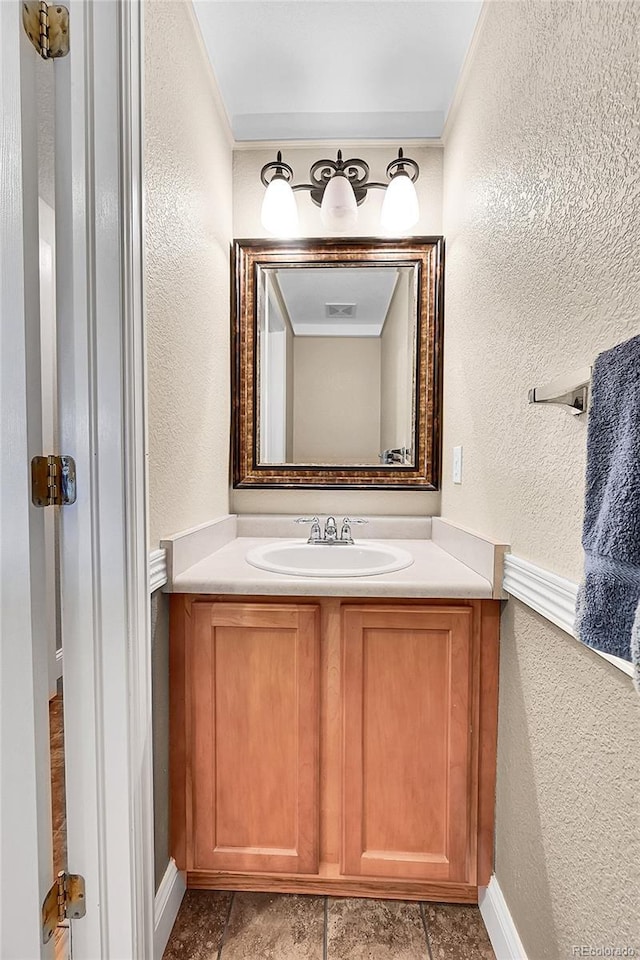 bathroom featuring visible vents, a textured wall, vanity, and baseboards