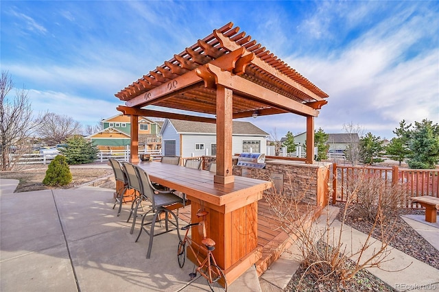 view of patio with grilling area, outdoor dry bar, an outbuilding, fence, and a pergola