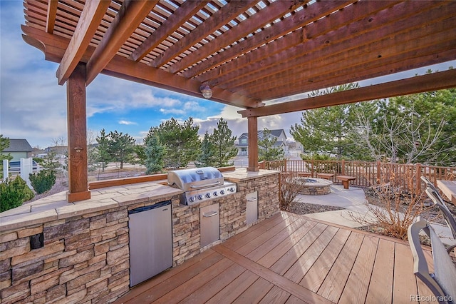 wooden deck with a grill, a fire pit, an outdoor kitchen, and a pergola